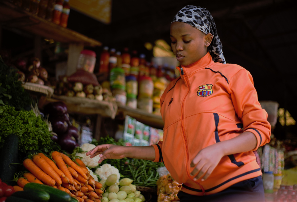 Rwandan lady standing in front of her vegetable stand